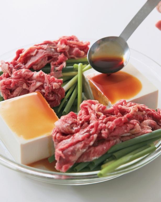 左右に豆腐を置き、中央以外のあいているところに万能ねぎを広げ、小麦粉をまぶした牛肉を均等に乗せる。「しみしみレンジ肉豆腐」 レシピ考案／小田真規子　撮影／澤木央子