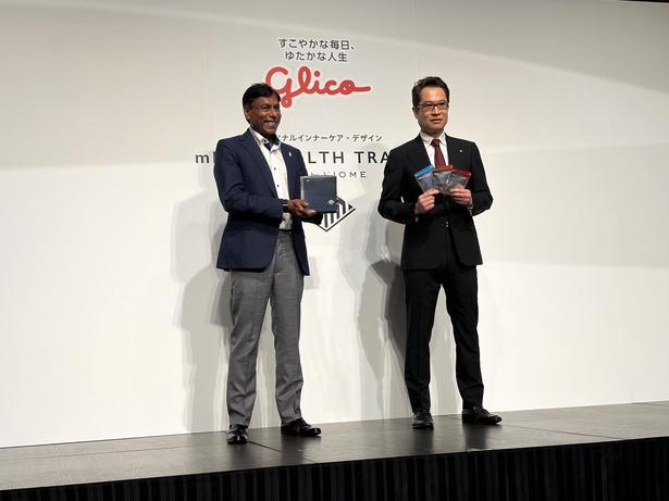 新サービス「mRNA HEALTH TRACKER」の検査キットを手に撮影に応じるジェインさん(左)と、江崎社長(右)